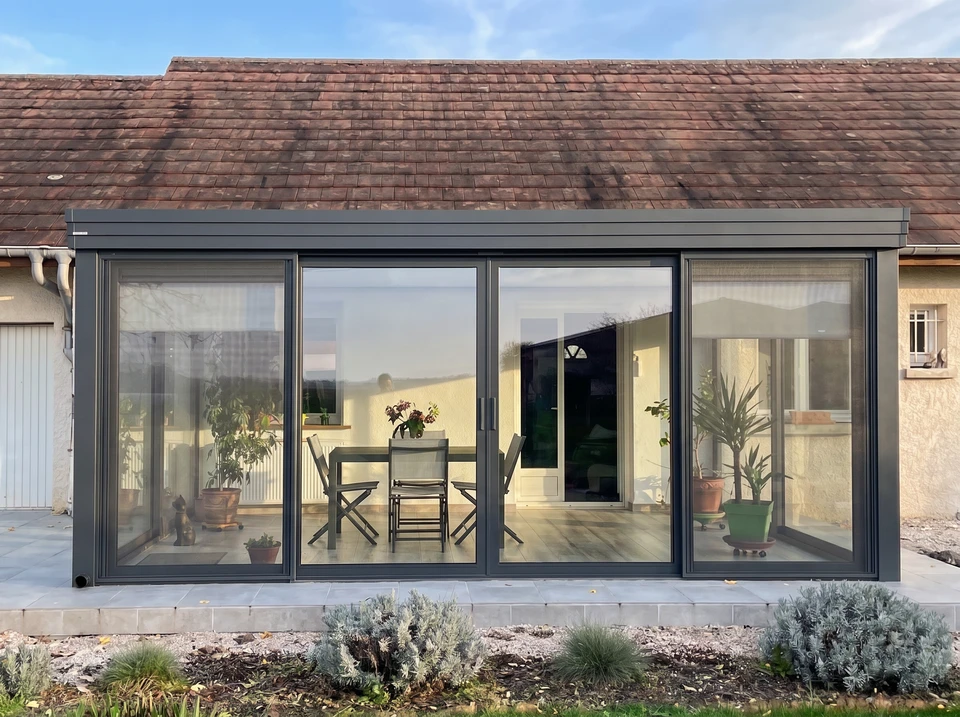 Façade en pierre calcaire avec une baie vitrée coulissante PVC blanc double vitrage, encadrée de volets battants bois peints vert amande (RAL 6021)